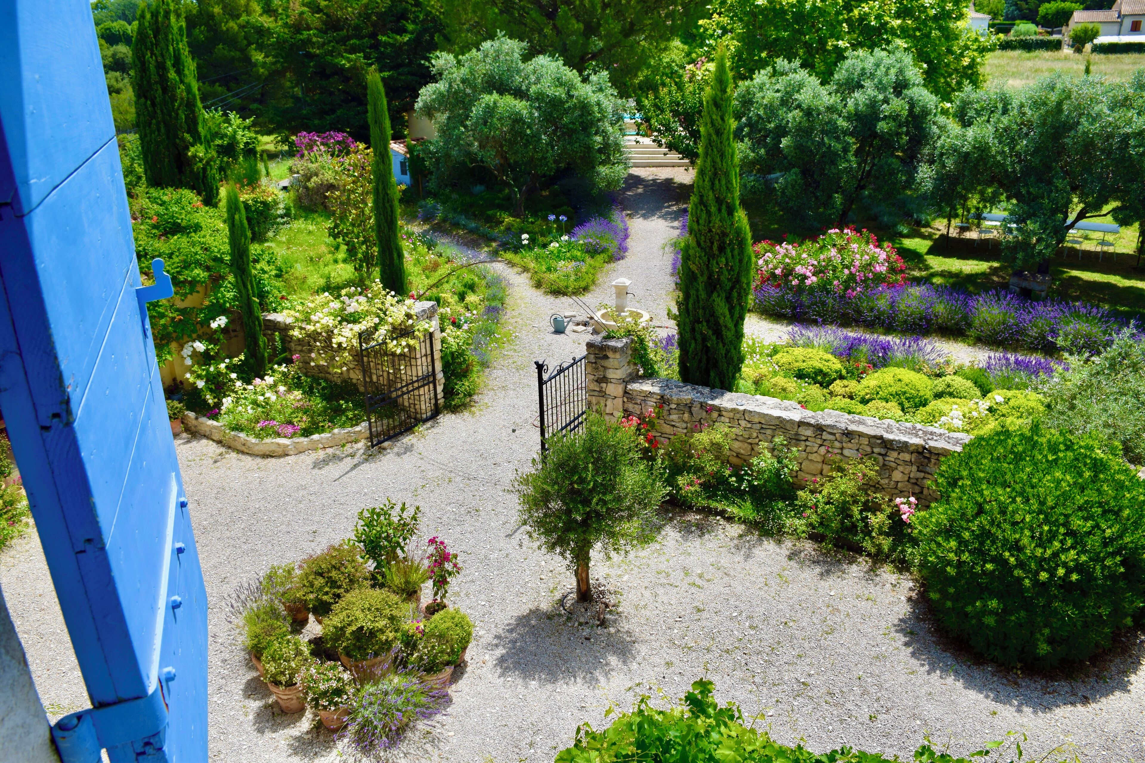 Un jardin avec un chemin de gravier, différentes plantes et un mur en pierre.