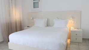 A neatly made bed with white linens, a bedside table with a lamp, and a nightstand with a phone. - Apanema Aegean Luxury Hotel (Mykonos)