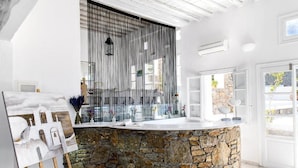 A modern bathroom with a stone counter, a large window with vertical blinds, and a painting on the wall. - Apanema Aegean Luxury Hotel (Mykonos)