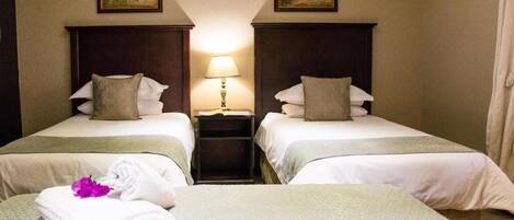 Una habitación de hotel con dos camas, una mesita de noche con lámpara y obras de arte en las paredes.