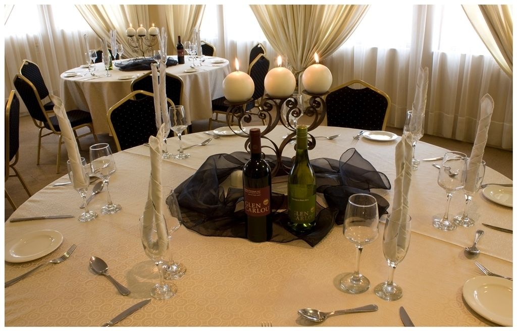 Una mesa de comedor dispuesta con copas de vino, platos y cubiertos, con velas y botellas de vino.