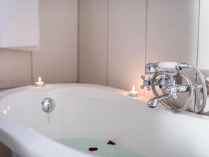Eine weiße Badewanne mit Duschbrause und einer Kerze am Rand.