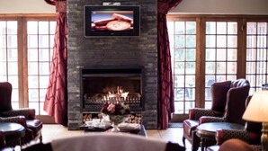 A cozy living room with a fireplace, comfortable seating, and a television mounted above it. - Alveston Manor (Middelburg)