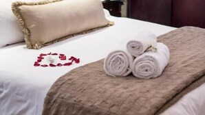 A neatly made bed with a fluffy beige blanket, a rolled towel, and a decorative red heart on the bedspread. - Alveston Manor (Middelburg)