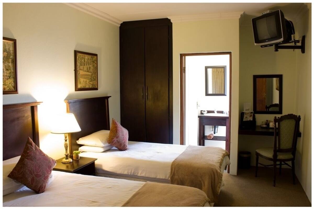 A hotel room with two beds, a desk, a chair, a television, and a wardrobe.