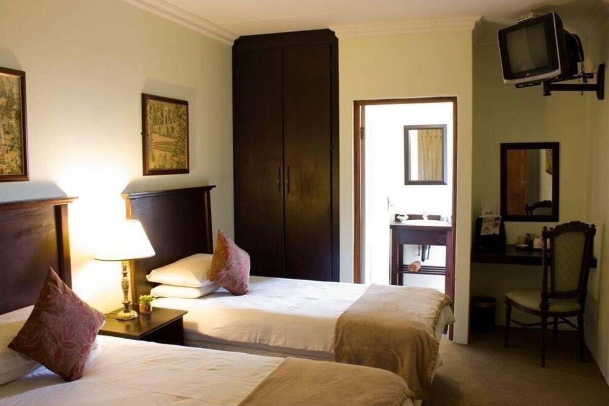 A hotel room with two beds, a desk, a chair, a television, and a wardrobe.
