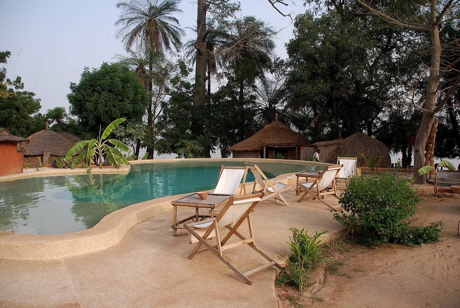 Ein Poolbereich mit Liegestühlen, einem Pool und strohgedeckten Hütten.