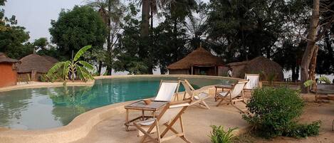 Ein Poolbereich mit Liegestühlen, einem Pool und strohgedeckten Hütten.
