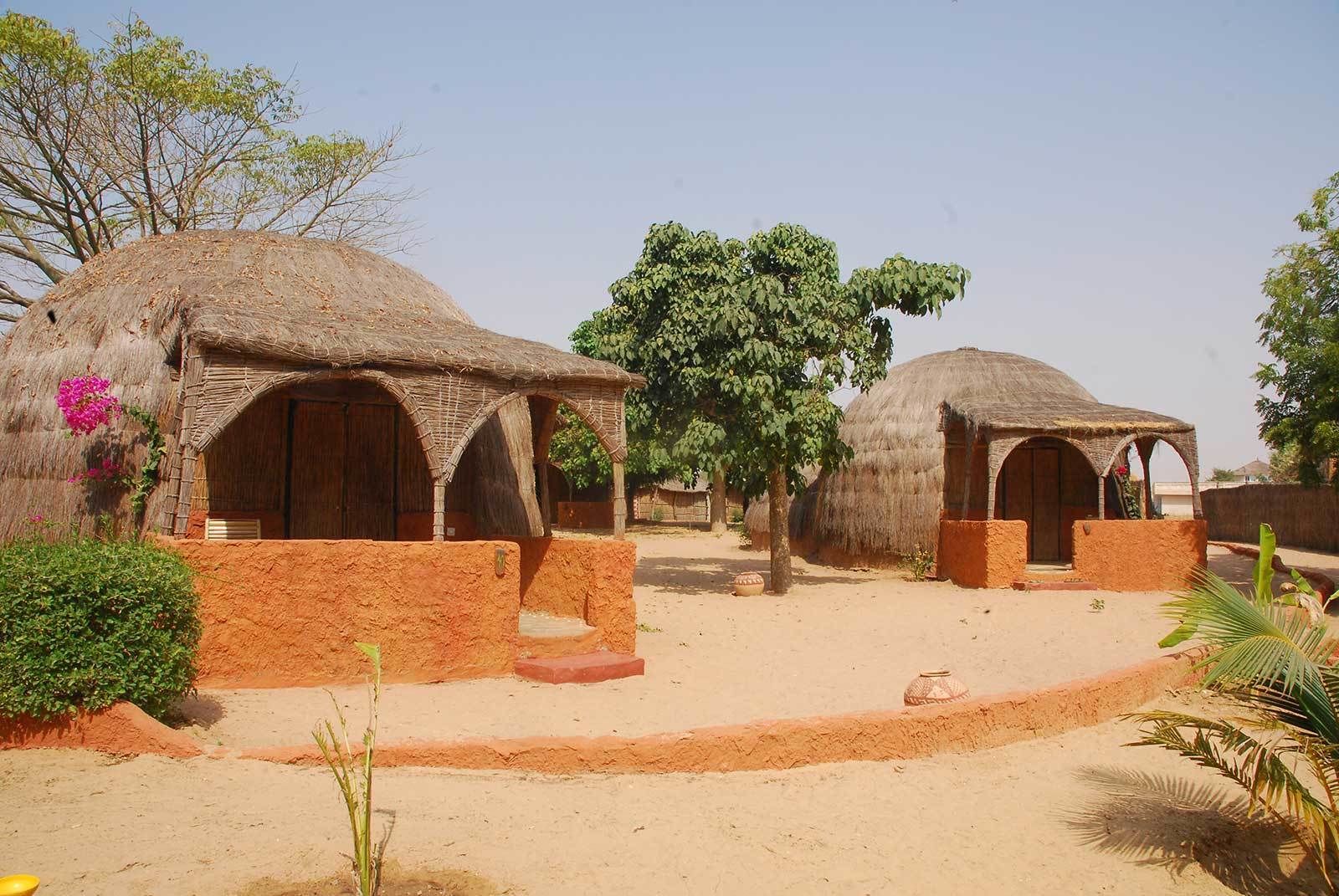 A traditional village with thatched-roof huts and a sandy ground.