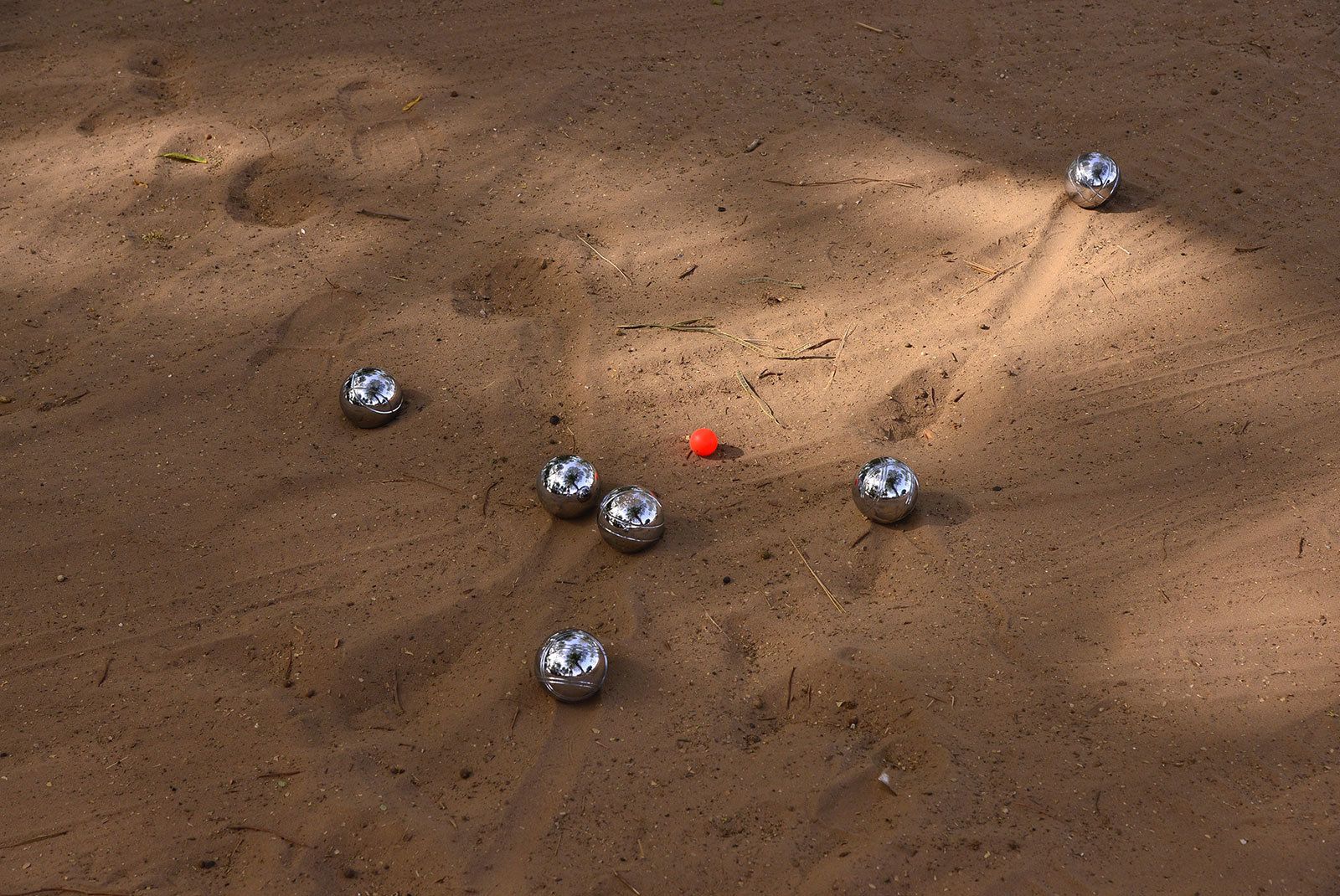 Terreno sabbioso con diverse sfere metalliche lucenti e una sfera rossa.