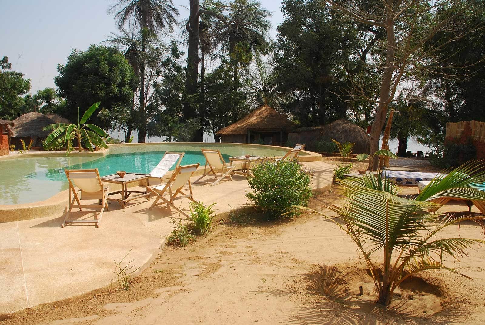 Uma área de piscina com espreguiçadeiras e uma estrutura com telhado de palha.