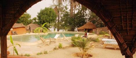 A pool area with lounge chairs and a thatched-roof structure.