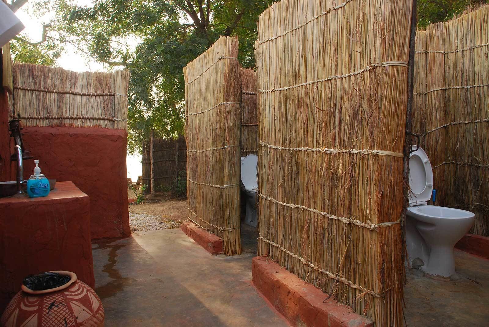 A rustic bathroom with thatched walls and a simple toilet setup.