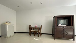 A room with a dining table, chairs, a refrigerator, and a cabinet with a television. - C.a.p. Mansion Hotel (Wichit)