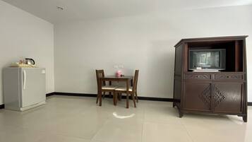 A room with a dining table, chairs, a refrigerator, and a cabinet with a television.