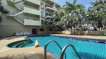 A swimming pool with a tiled edge, a multi-story building with balconies, and palm trees.