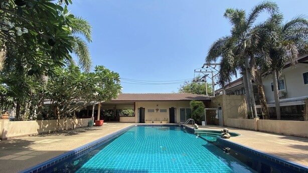 A swimming pool with tiled edges, surrounded by palm trees and a building with a tiled roof. - C.a.p. Mansion Hotel (Wichit)