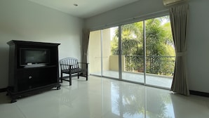 A spacious room with a sliding glass door leading to a balcony, a dark-colored entertainment unit, and a single chair. - C.a.p. Mansion Hotel (Wichit)