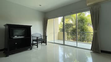 A spacious room with a sliding glass door leading to a balcony, a dark-colored entertainment unit, and a single chair.