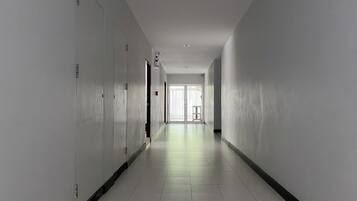 A long, narrow hallway with white walls and a tiled floor, leading to a door at the end.