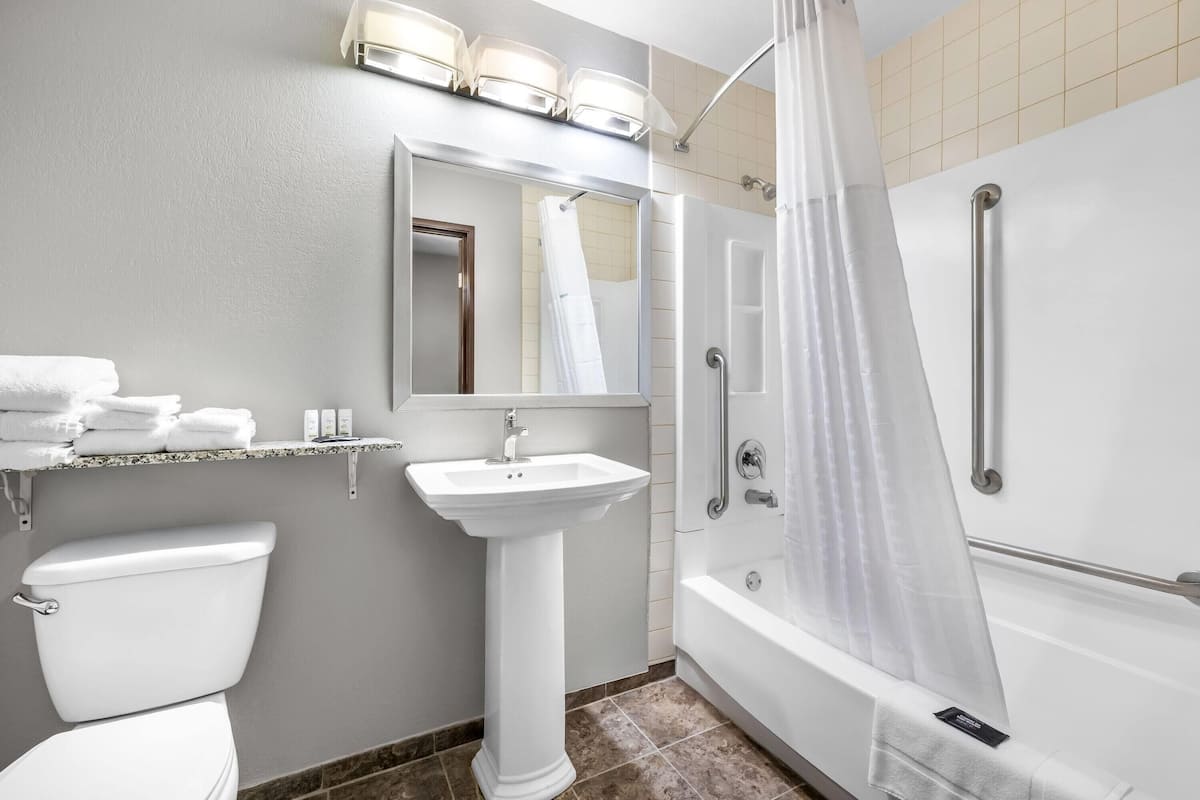 A bathroom with a toilet, pedestal sink, mirror, shower, and bathtub.