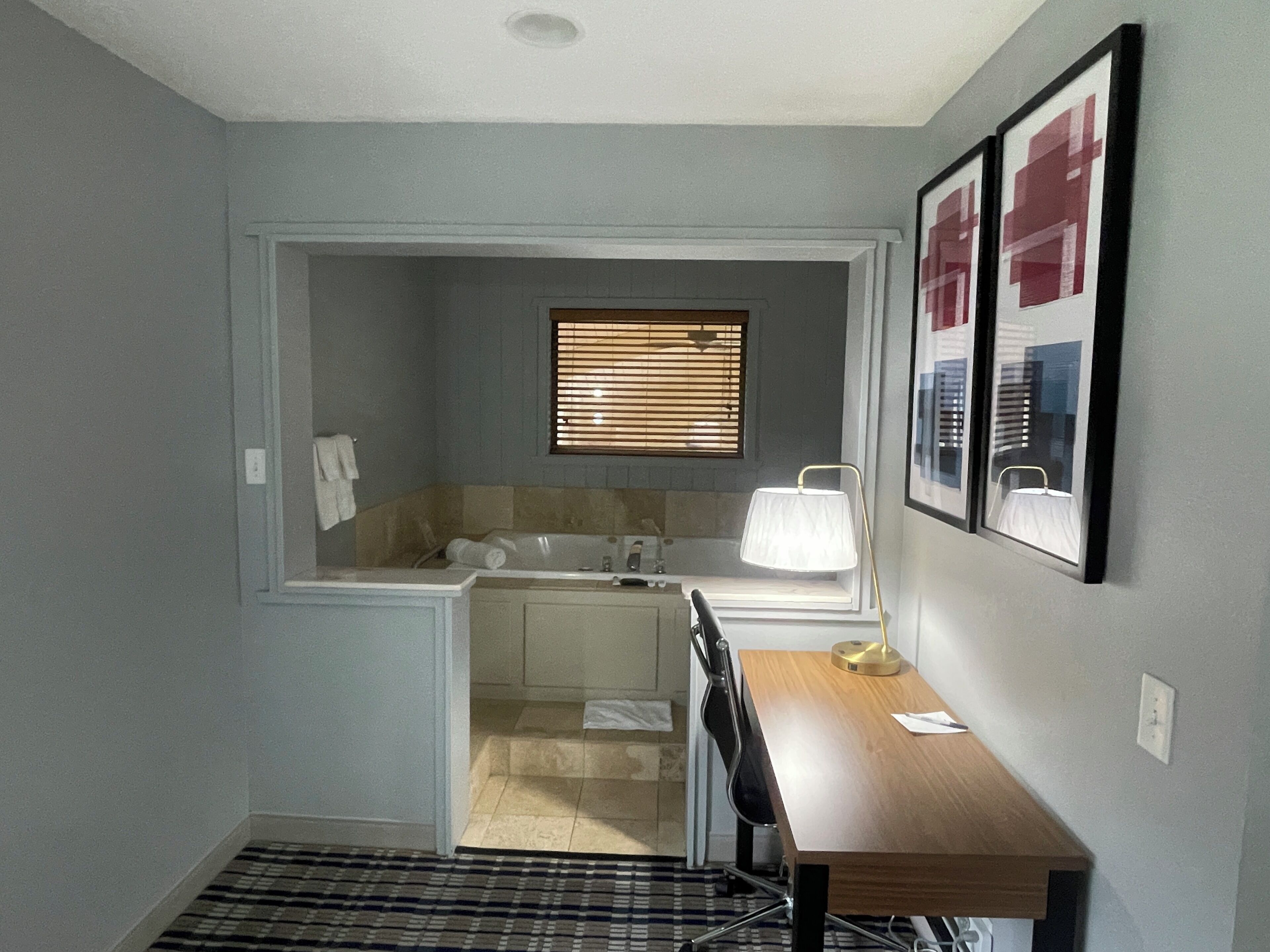 A compact bathroom with a bathtub, a sink, and a toilet. There is a window with blinds, a towel rack, and a framed picture on the wall.