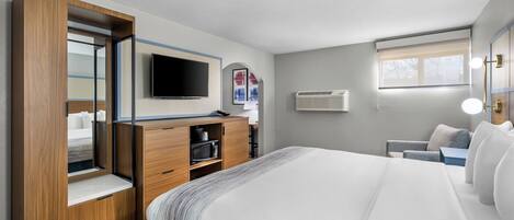 A hotel room with a bed, a TV, a desk with a computer, a wardrobe, and a window.