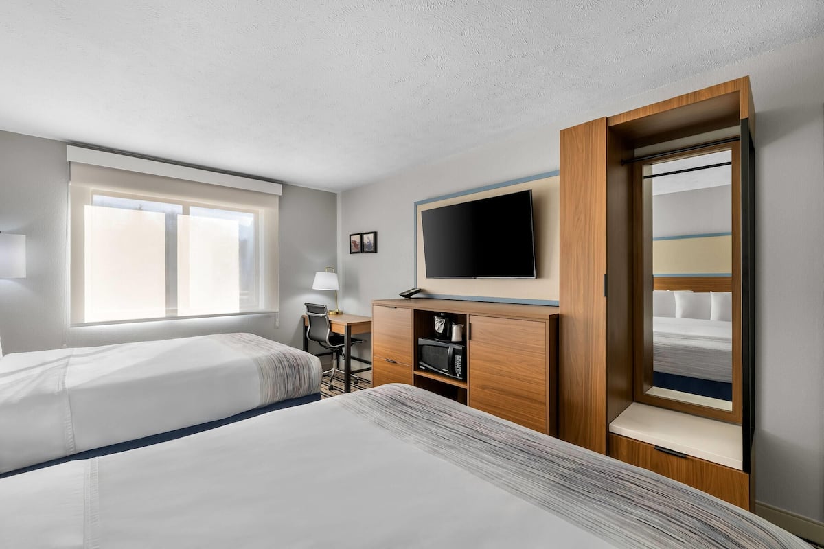 A hotel room with two beds, a desk, a TV, and a wardrobe.