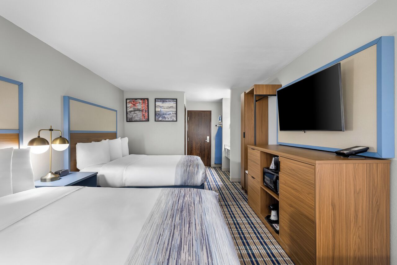 A hotel room with two beds, a TV, a desk with a lamp, and a wardrobe.