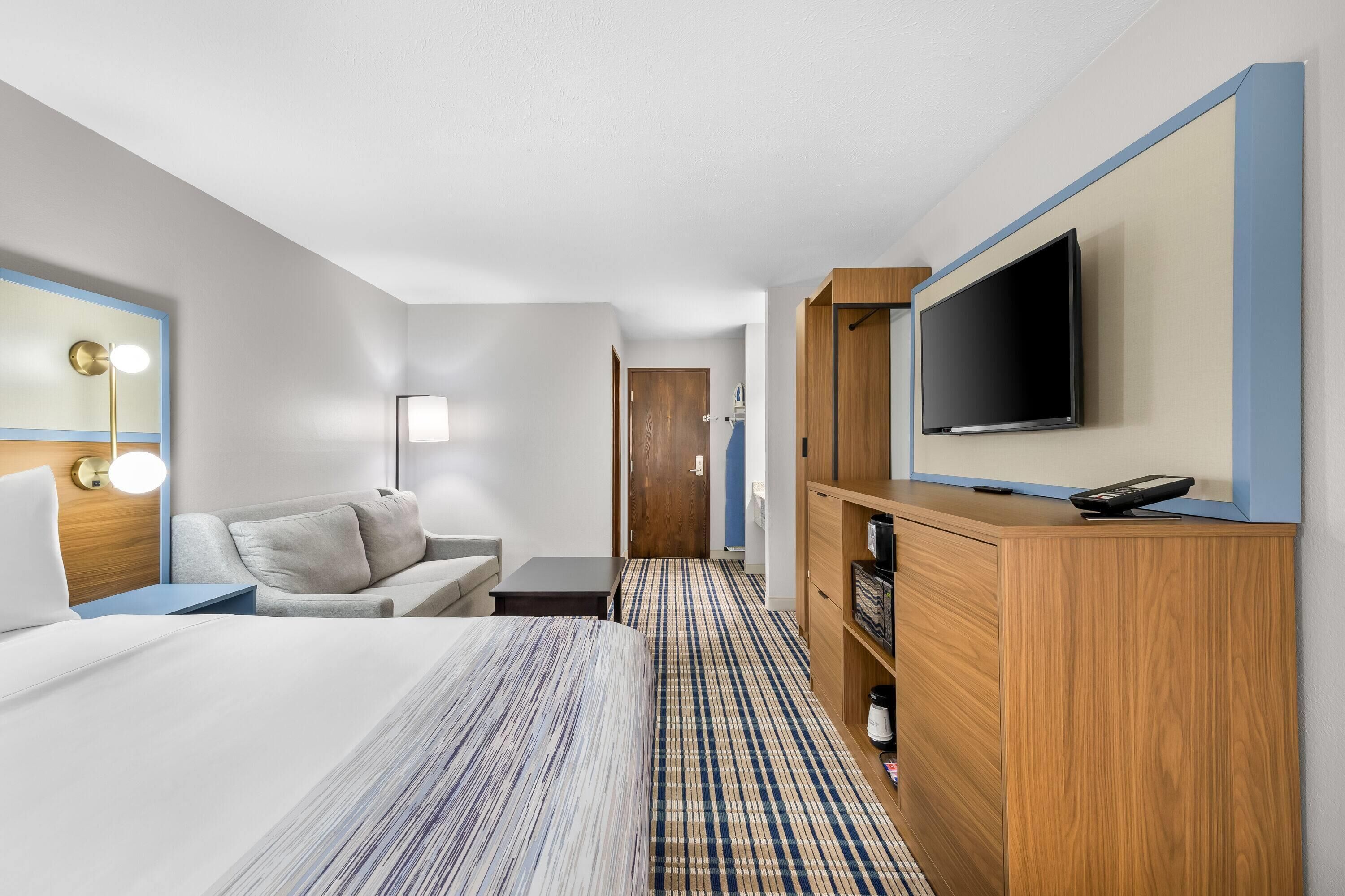 A hotel room with a bed, a desk, a TV, a sofa, and a wooden cabinet.