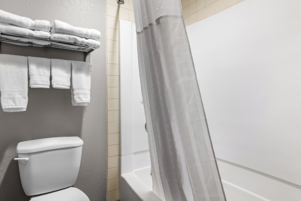 A bathroom with a toilet, a towel rack with folded towels, and a shower curtain.