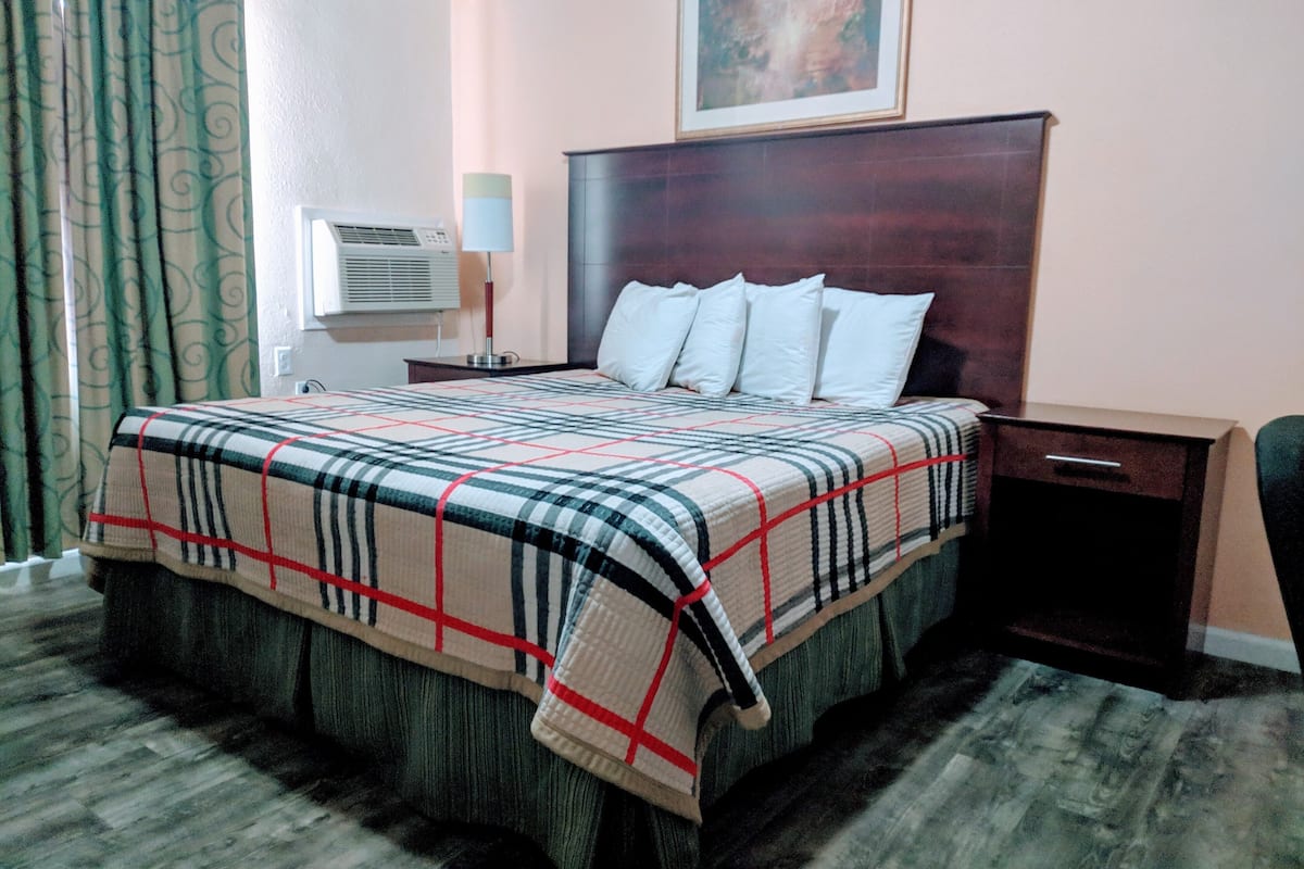 A hotel room with a large bed, a nightstand, a desk, and a chair.