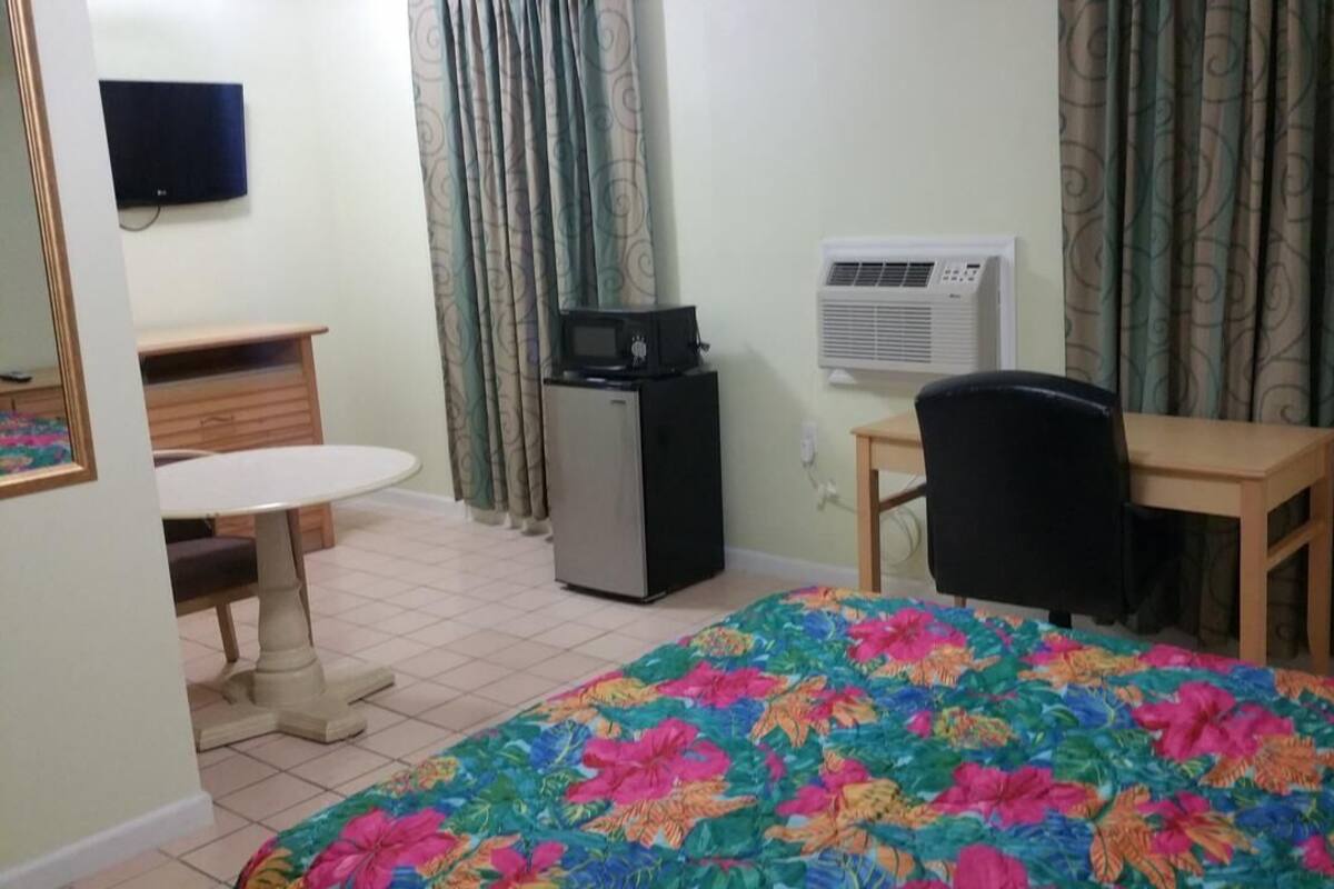 A hotel room with a bed, a desk, a chair, a television, an air conditioner, and curtains.