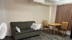 A room with a striped sofa, two wooden chairs, a round table, and a standing fan.