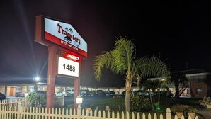 A hotel with a signboard displaying the name 'Travelers' and a contact number. There is a white picket fence in the foreground.