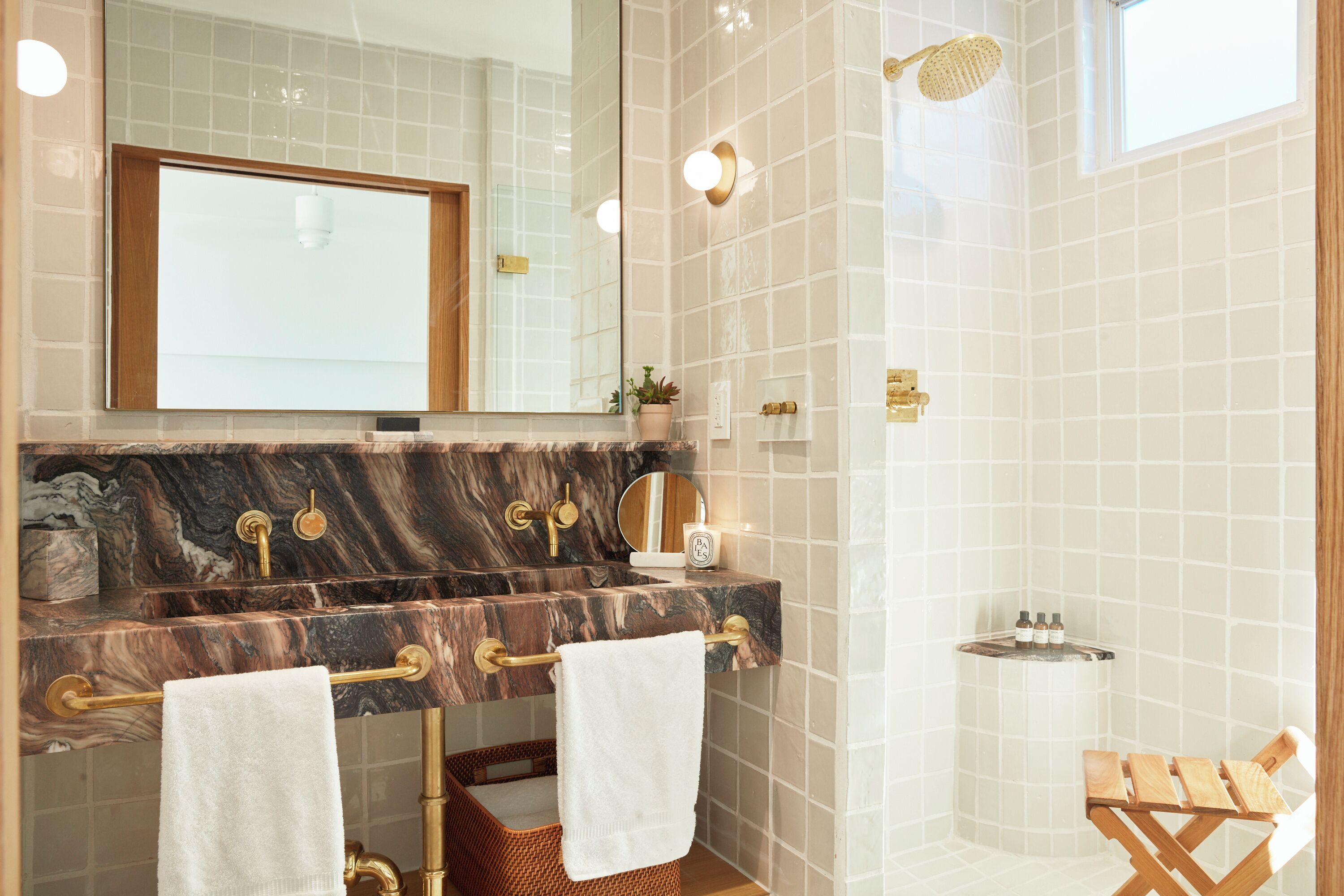 A bathroom with a marble sink, gold fixtures, a mirror, and a shower.
