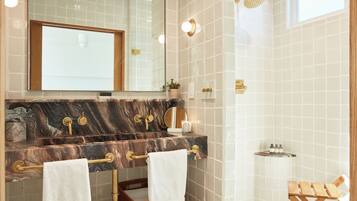A bathroom with a marble sink, gold fixtures, a mirror, and a shower.