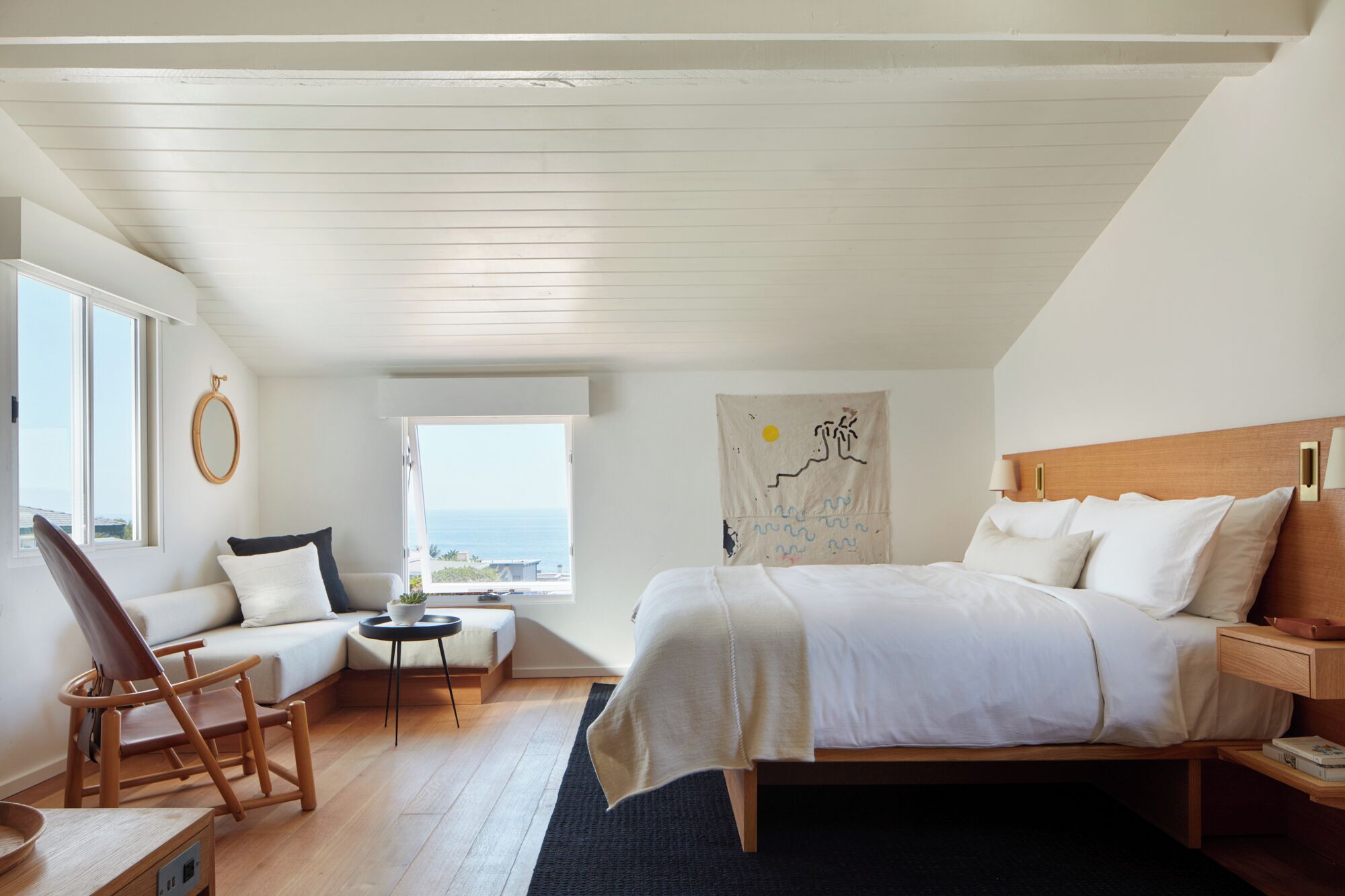 A bedroom with a bed, a chair, a small table, a window with a view, and a wall with a tapestry.