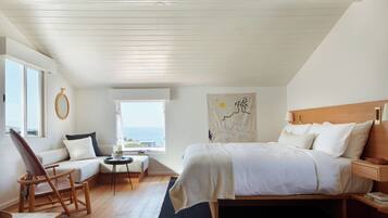A bedroom with a bed, a chair, a small table, a window with a view, and a wall with a tapestry.