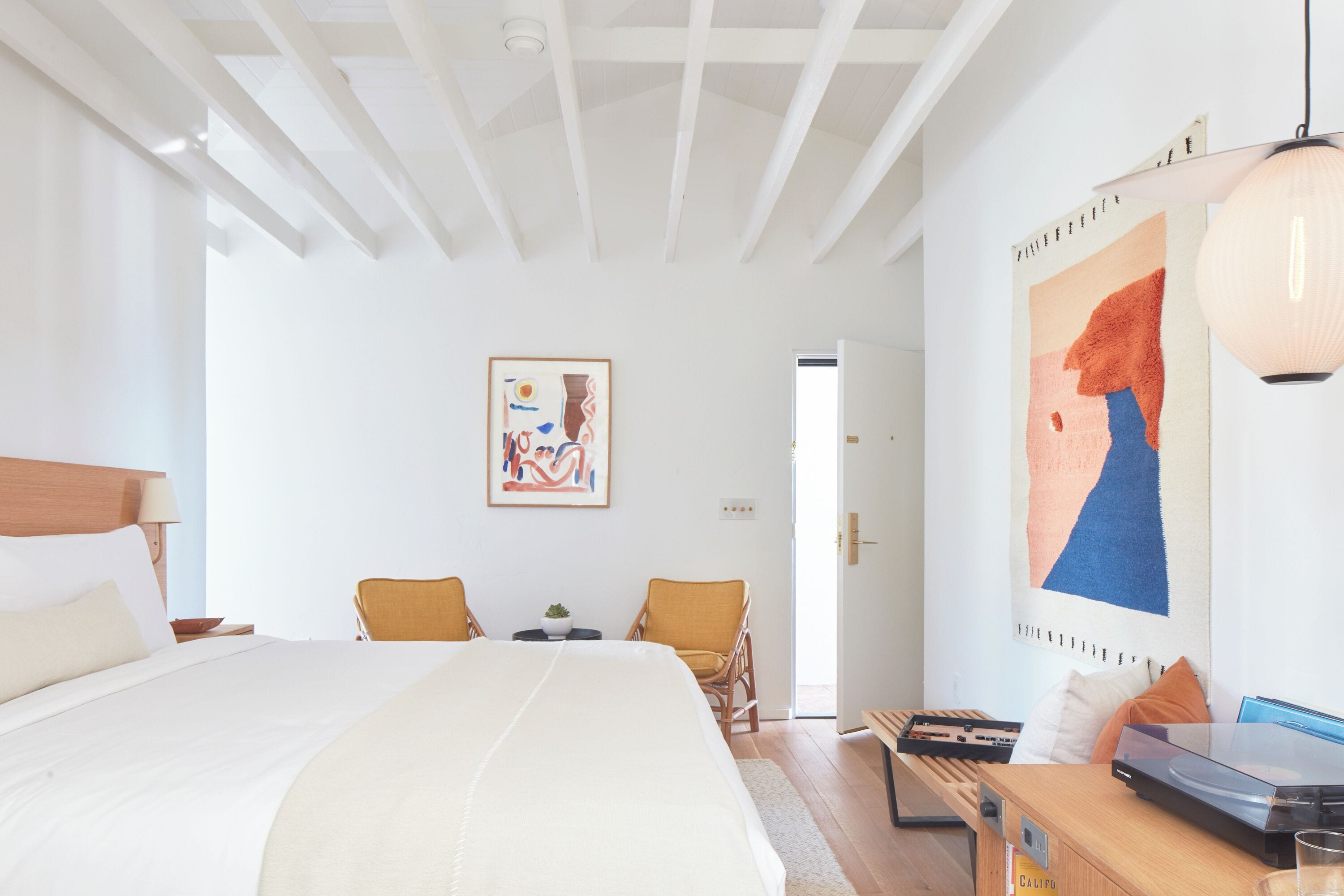 A spacious bedroom with a large bed, a desk, two chairs, and artwork on the walls.