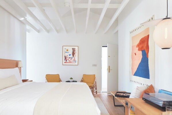 A spacious bedroom with a large bed, a desk, two chairs, and artwork on the walls. - Hotel Joaquin (Laguna Beach)