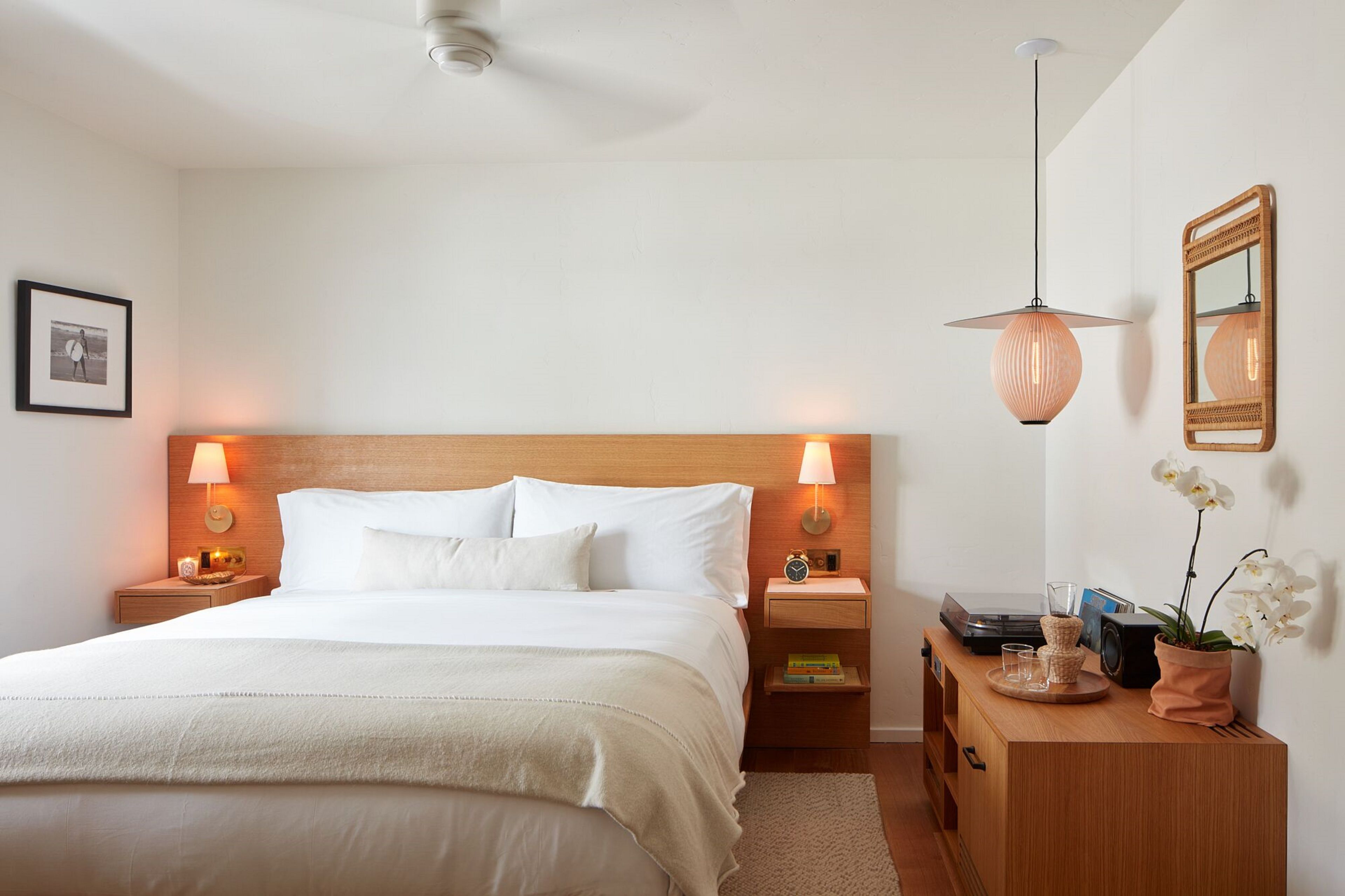 Un dormitorio ordenado con una cama grande, lámparas de noche, una mesita de madera, un aparador y un espejo en la pared.