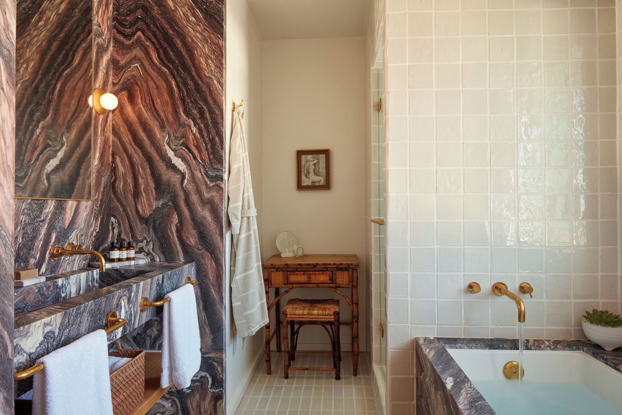 A bathroom with a marble vanity, a wooden bench, a framed picture on the wall, and a bathtub with a tiled shower area.