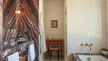 A bathroom with a marble vanity, a wooden bench, a framed picture on the wall, and a bathtub with a tiled shower area.