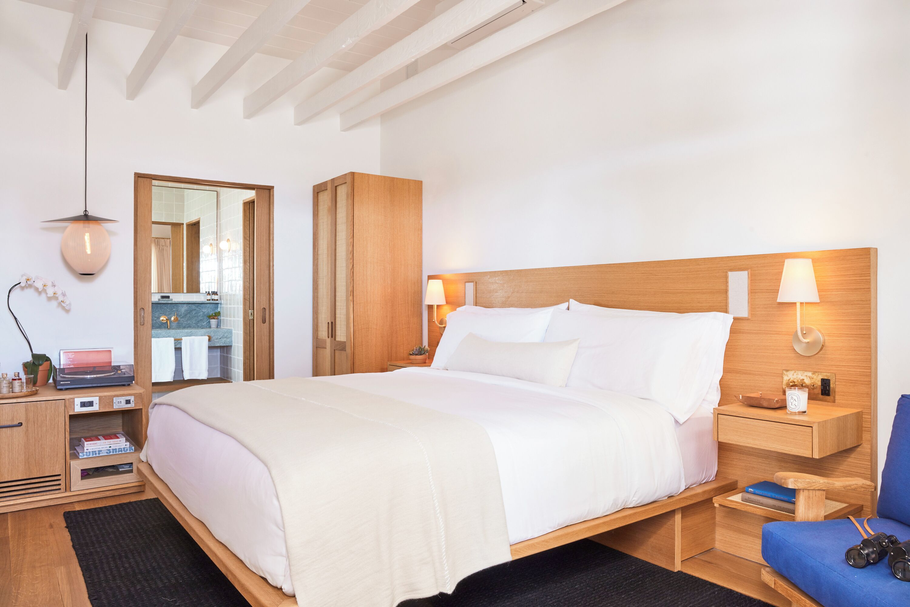 Een hotelkamer met een groot bed, een houten hoofdbord, nachtkastjes, een spiegel en een zithoekje.