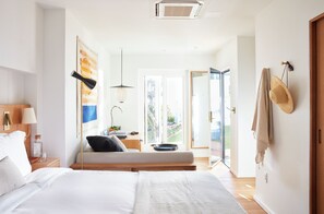 A modern hotel room with a bed, bedside table, lamp, and a view of the outdoors. - Hotel Joaquin (Laguna Beach)