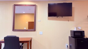 Une chambre d’hôtel dotée d’un grand miroir, d’un téléviseur à écran plat, d’un four à micro-ondes, d’une table en bois et d’un fauteuil de bureau noir.