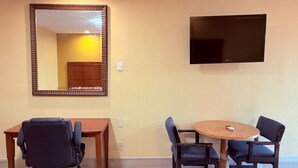 Une salle de conférence avec une table en bois, deux chaises, un grand miroir et un téléviseur à écran plat fixé au mur.