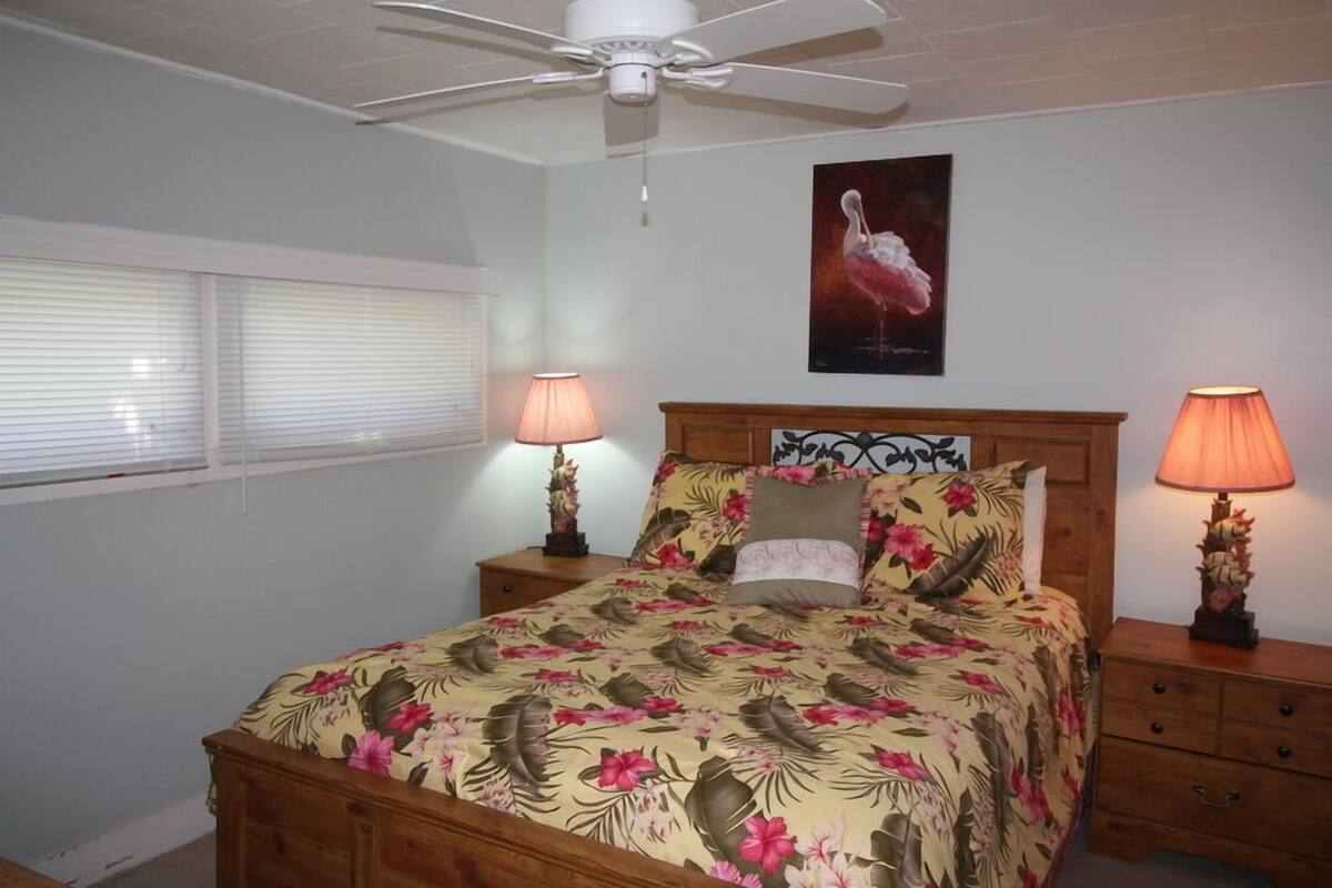 Een slaapkamer met een bed, twee nachtkastjes, een plafondventilator en een schilderij aan de muur.