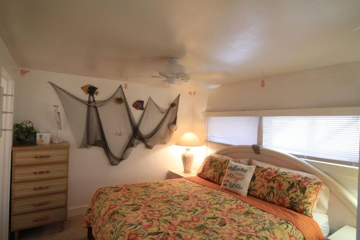 Een slaapkamer met een bed, een kaptafel, een lamp en een plafondventilator.